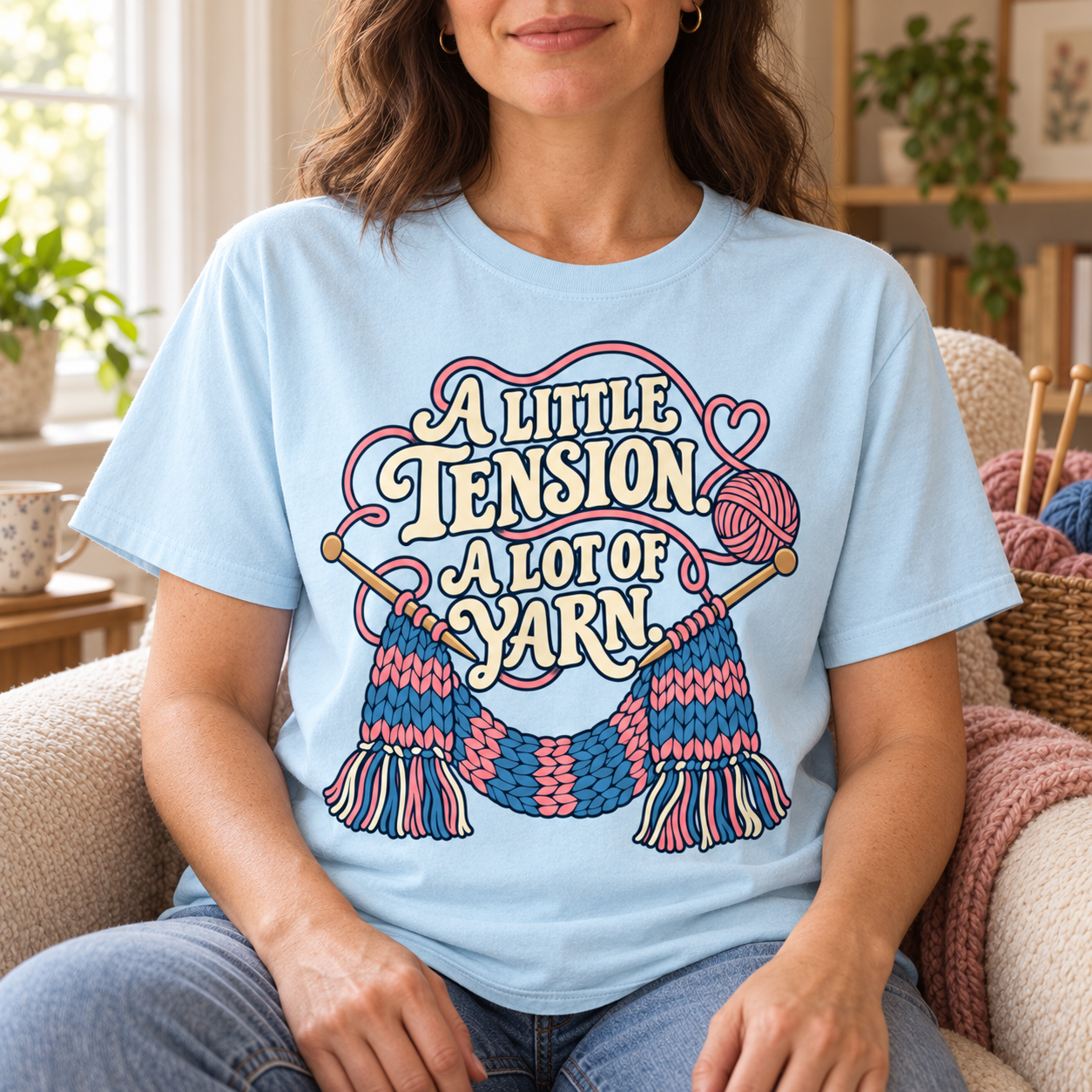 Woman wearing the A Little Tension A Lot of Yarn tee beside knitting materials
