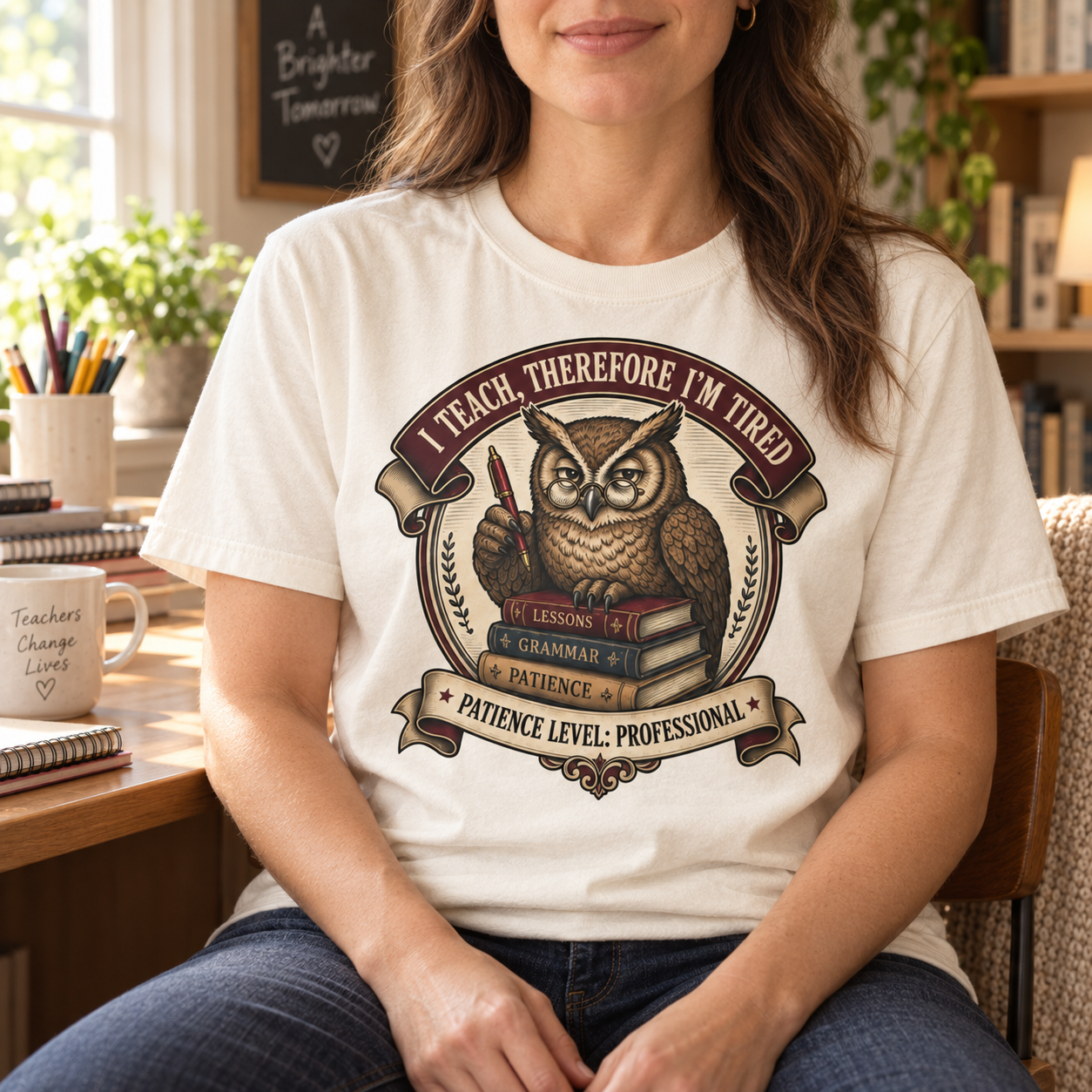 Woman wearing the I Teach Therefore I Am Tired owl tee beside a desk